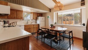 A kitchen with wooden cabinets, a white countertop, a dining table with chairs, and a large window. - Three bedroom  in United States of America, Big Bear (Big Bear)