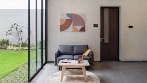 A modern room with a grey sofa, a wooden coffee table, and a large window. - Cove Legacy (Jakarta)