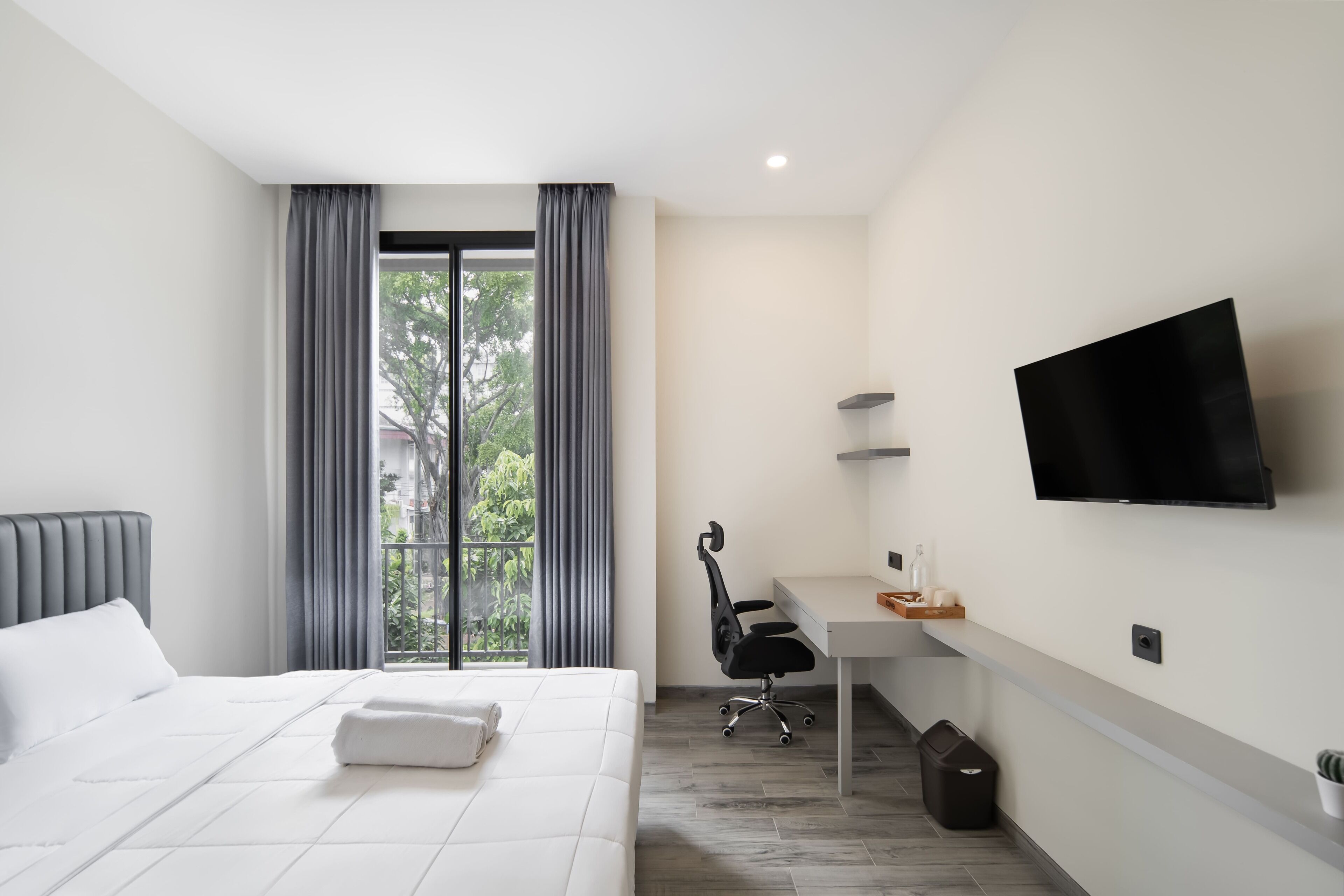 Een moderne hotelkamer met een groot bed, een bureau, een stoel, een televisie en uitzicht op groen.