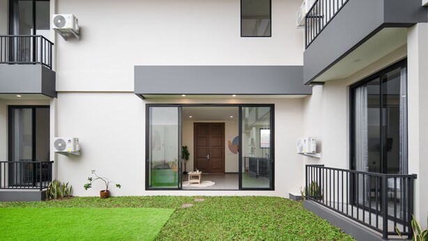 A modern two-story building with a flat roof, large sliding glass doors, and a small garden area with grass and potted plants. - Cove Legacy (Jakarta)