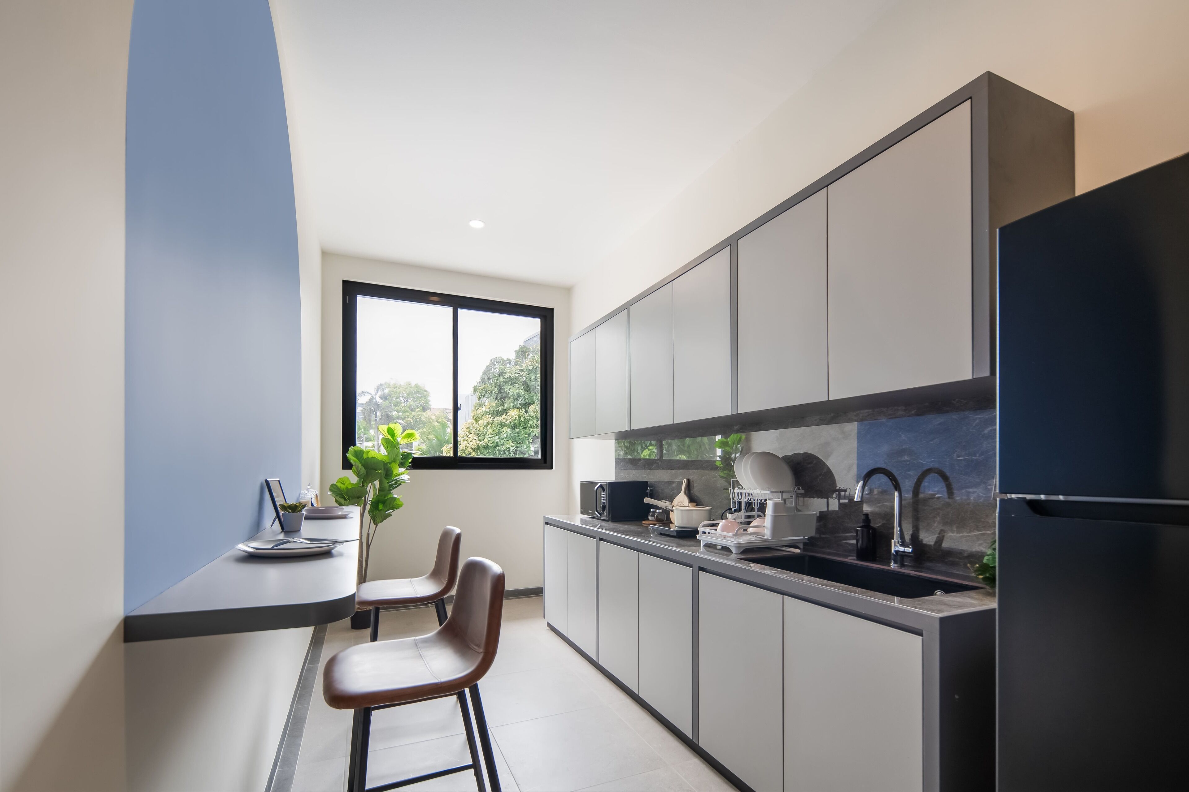 Une cuisine moderne avec des meubles gris, un réfrigérateur noir et une fenêtre donnant sur un paysage verdoyant.