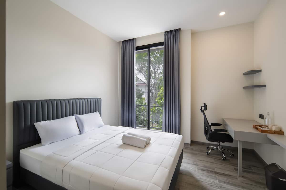 Quarto de hotel moderno com uma cama grande, uma escrivaninha e vista para o exterior.