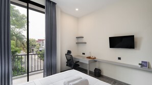 A hotel room with a bed, a desk, a chair, a TV, and a balcony with curtains. - Cove Legacy (Jakarta)