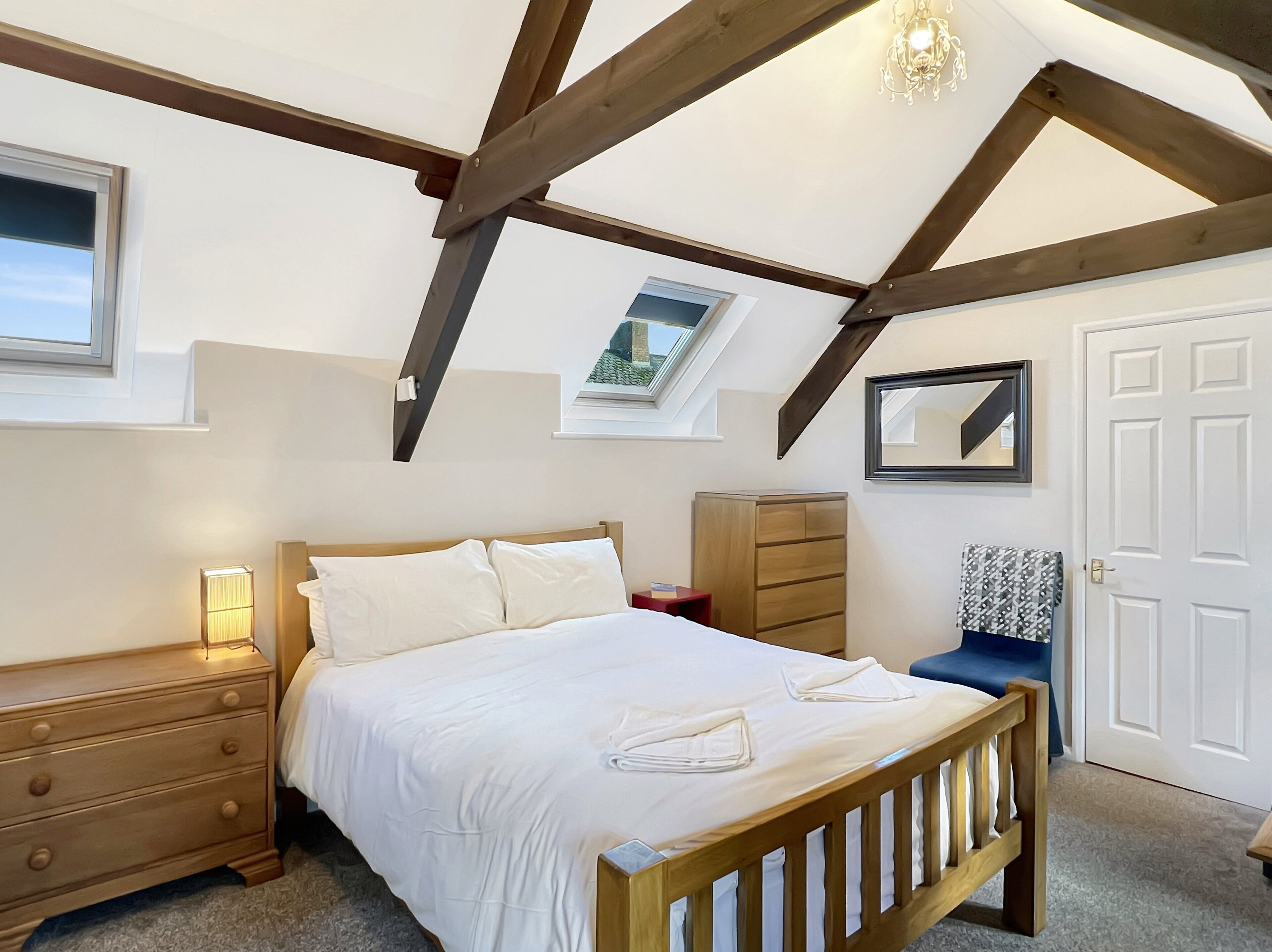 Een slaapkamer met een houten bed, een nachtkastje, een kaptafel, een spiegel en een dakraam.