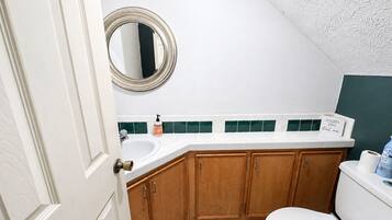 Un baño con un lavamanos blanco, armarios de madera, un inodoro y un espejo.