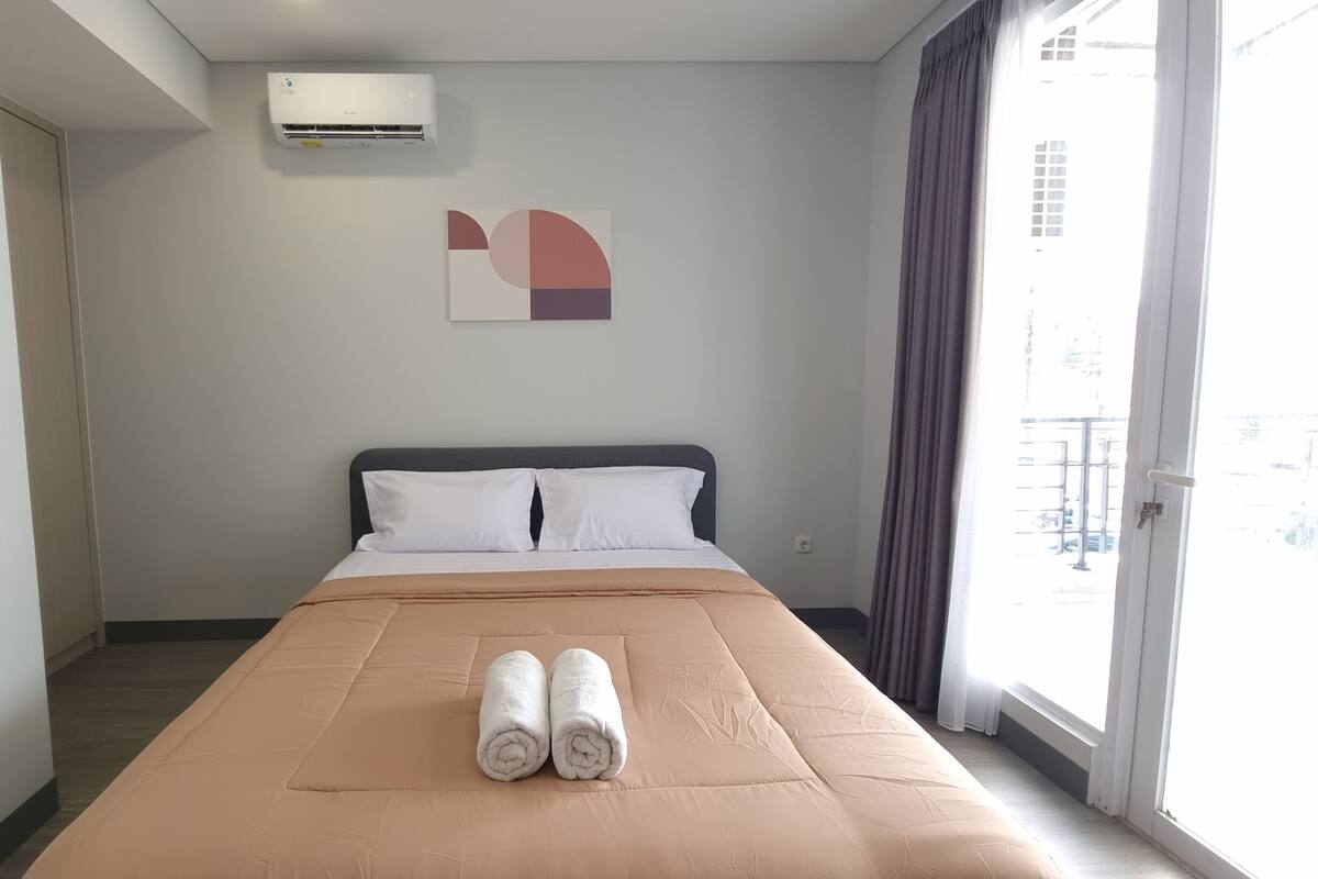 A hotel room with a bed, a window, and an air conditioning unit.