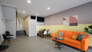 A modern office space with a reception desk, a seating area with an orange sofa, and a staircase leading to an upper level. - Cove Anasera (South Tangerang)