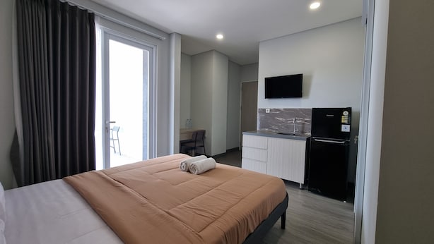 A hotel room with a large bed, a small kitchenette, a flat-screen TV, and a sliding door to a balcony. - Cove Anasera (South Tangerang)