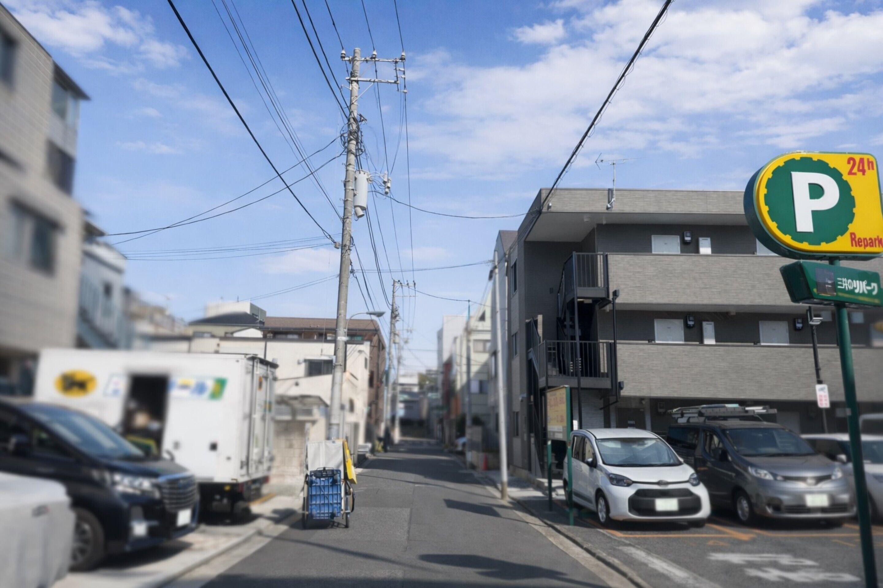 A street with parked cars and a 24-hour parking sign.