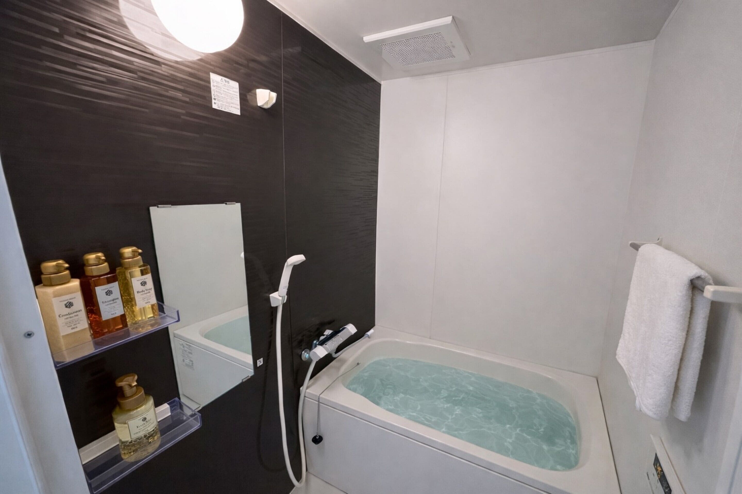 A modern bathroom with a bathtub, a white towel hanging on the wall, and shelves with toiletries.