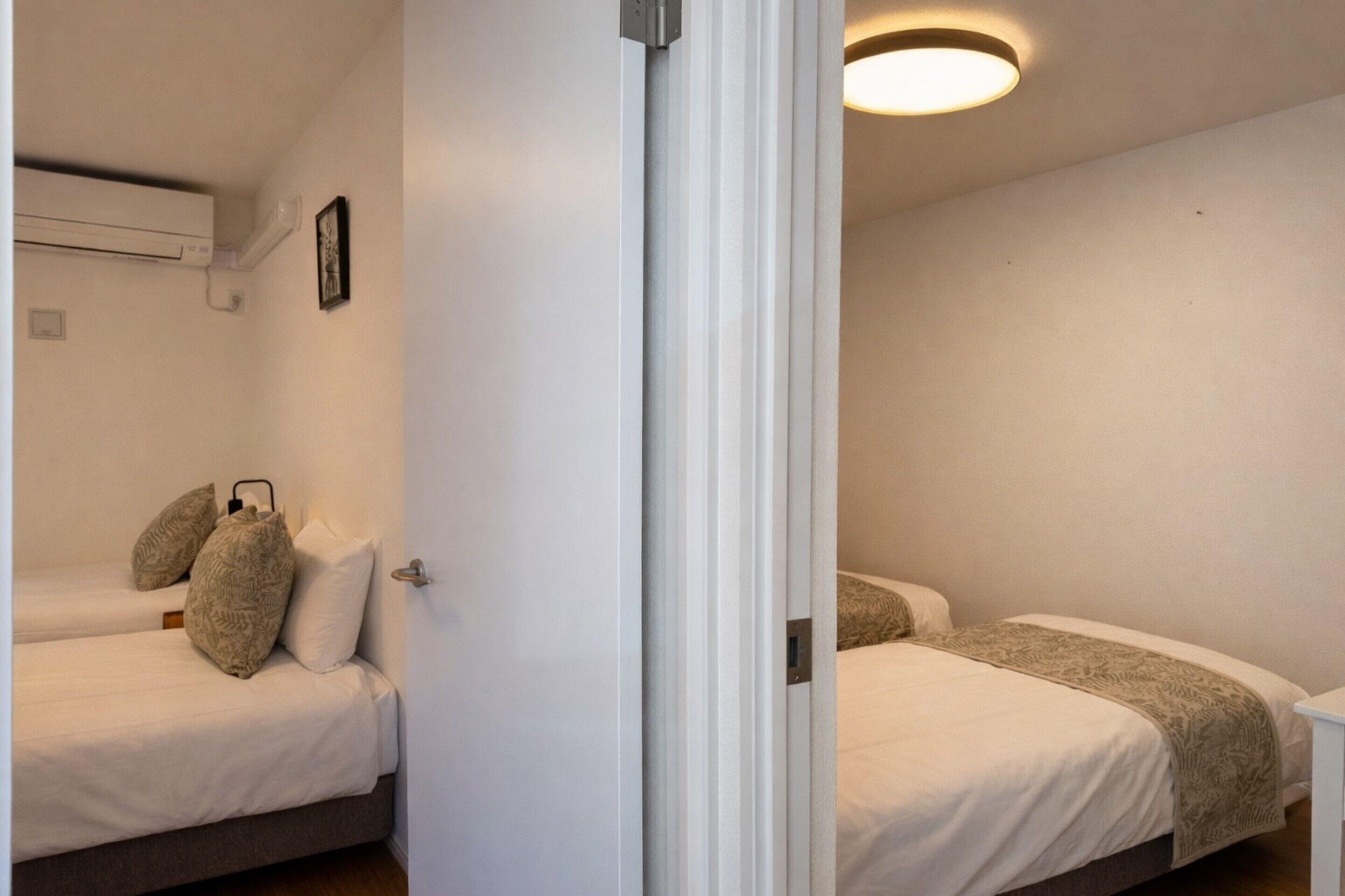 Una habitación con dos camas, una puerta blanca e iluminación en el techo.