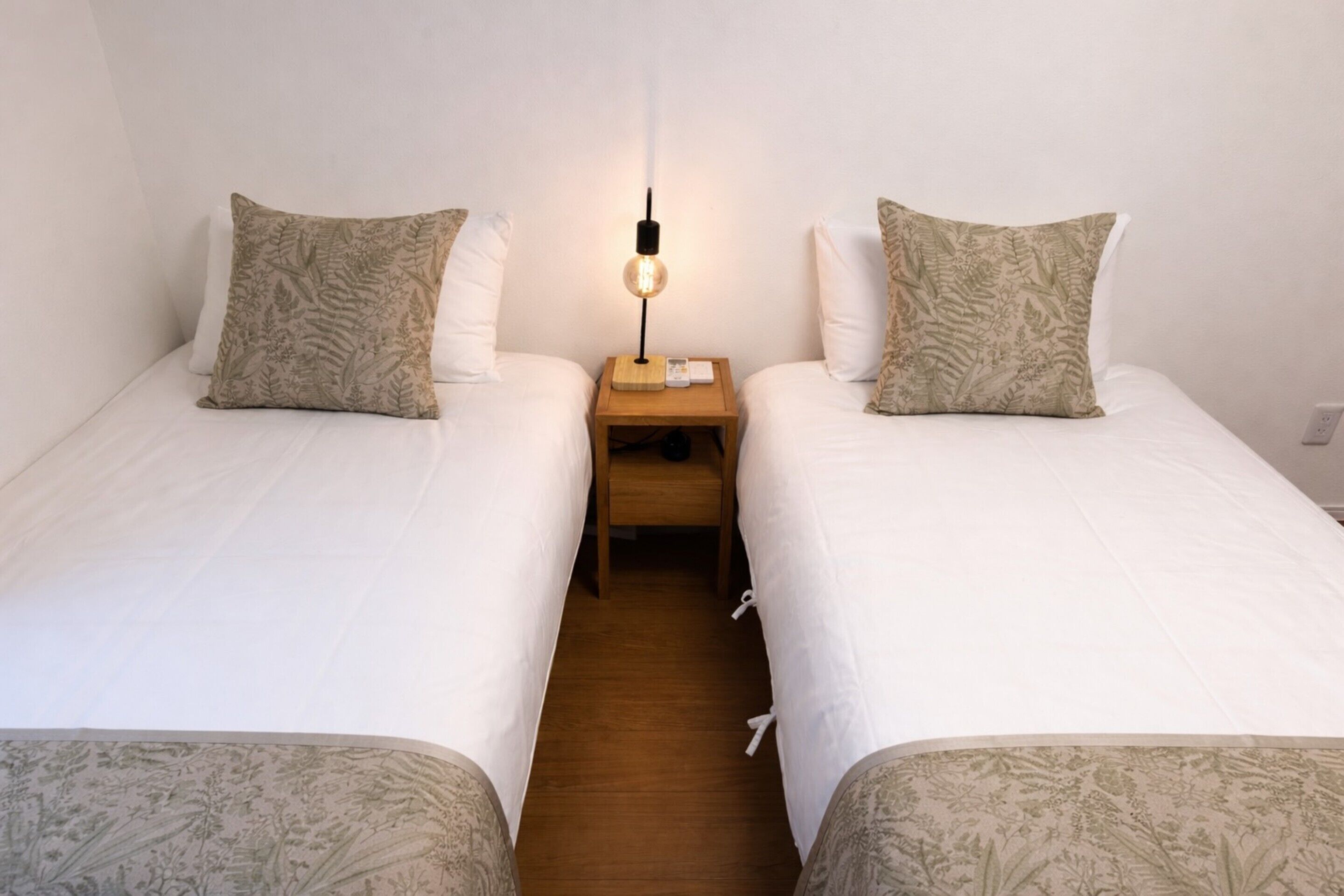 A twin room with two beds, a nightstand with a lamp, and a wooden floor.