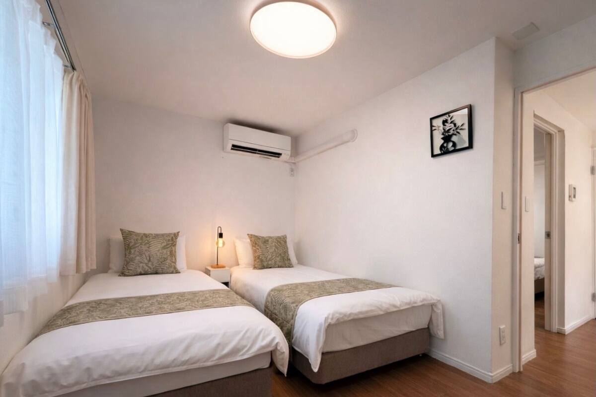 A bedroom with two beds, a bedside lamp, an air conditioning unit, and a framed picture on the wall.