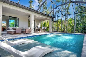 A modern outdoor swimming pool area with a glass-enclosed patio, lounge chairs, and a view of the surrounding forest. - The Sanctuary: Bonita Springs Pool Home (Bonita Springs)