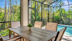 Zona pranzo con tavolo e sedie, ampie finestre vista foresta e piscina.