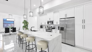 A modern kitchen with white cabinets, stainless steel appliances, and a marble countertop. - Coral Waters Modern Escape | Pool Home (Cape Coral)