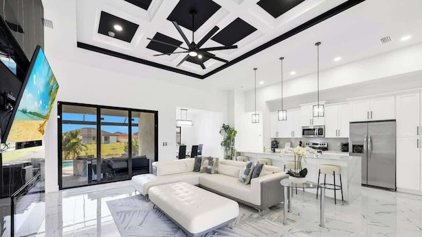 A modern living room with a sectional sofa, a flat-screen TV, and a dining area with a glass door leading to a balcony. - Coral Waters Modern Escape | Pool Home (Cape Coral)