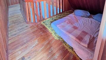 A wooden-floored room with a bed, a wooden railing, and a patterned rug.