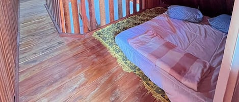 A wooden-floored room with a bed, a wooden railing, and a patterned rug.