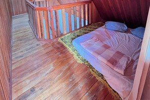 Une pièce au plancher de bois, avec un lit, une rambarde en bois et un tapis à motifs.