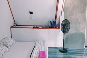 Une chambre à coucher comprenant un lit, une table de chevet, un ventilateur et une étagère murale sur laquelle sont disposés divers objets.