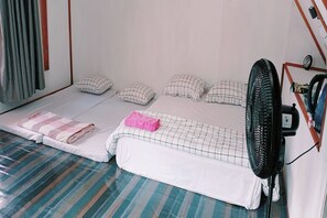 Un lit simple avec un matelas à rayures, un ventilateur et une fenêtre avec des rideaux.