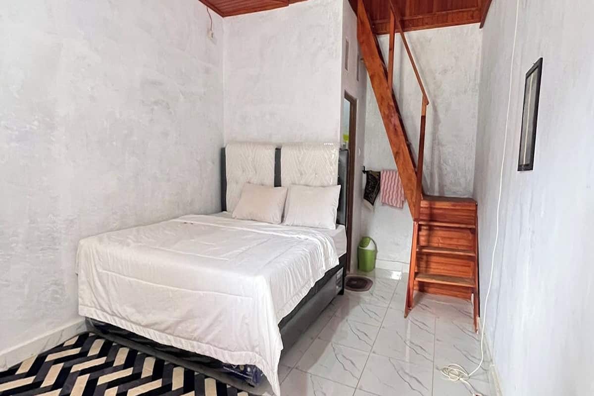 Un dormitorio con una cama, una escalera de madera y un cubo de basura verde pequeño.