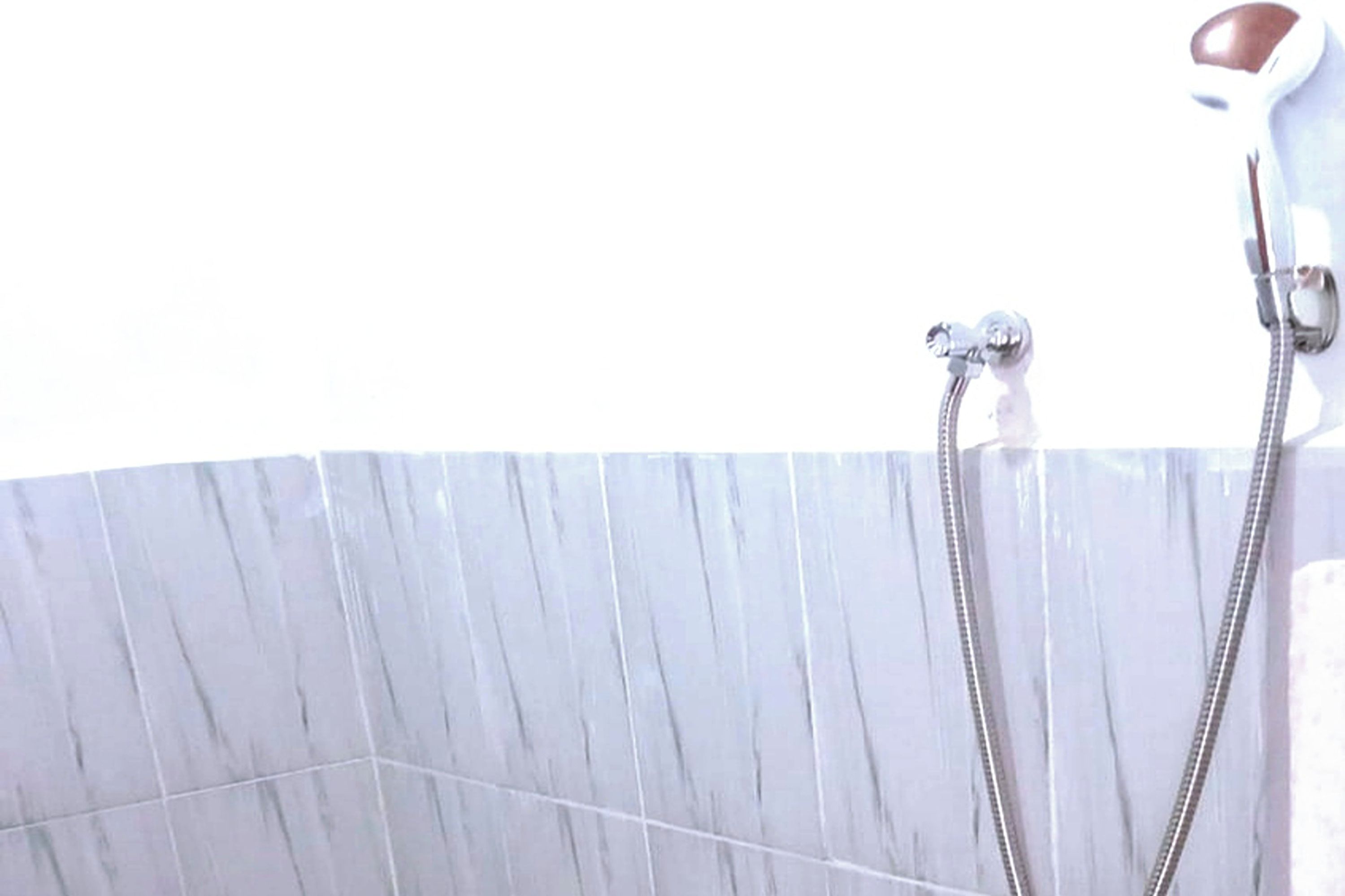 A bathroom with a marble wall and a shower with a handheld showerhead.