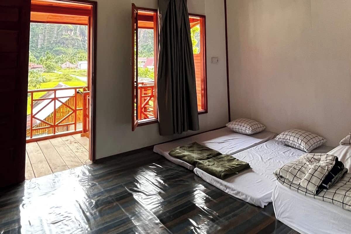 Habitación con dos camas, vistas a una terraza de madera y follaje exterior, y una cortina en una ventana.