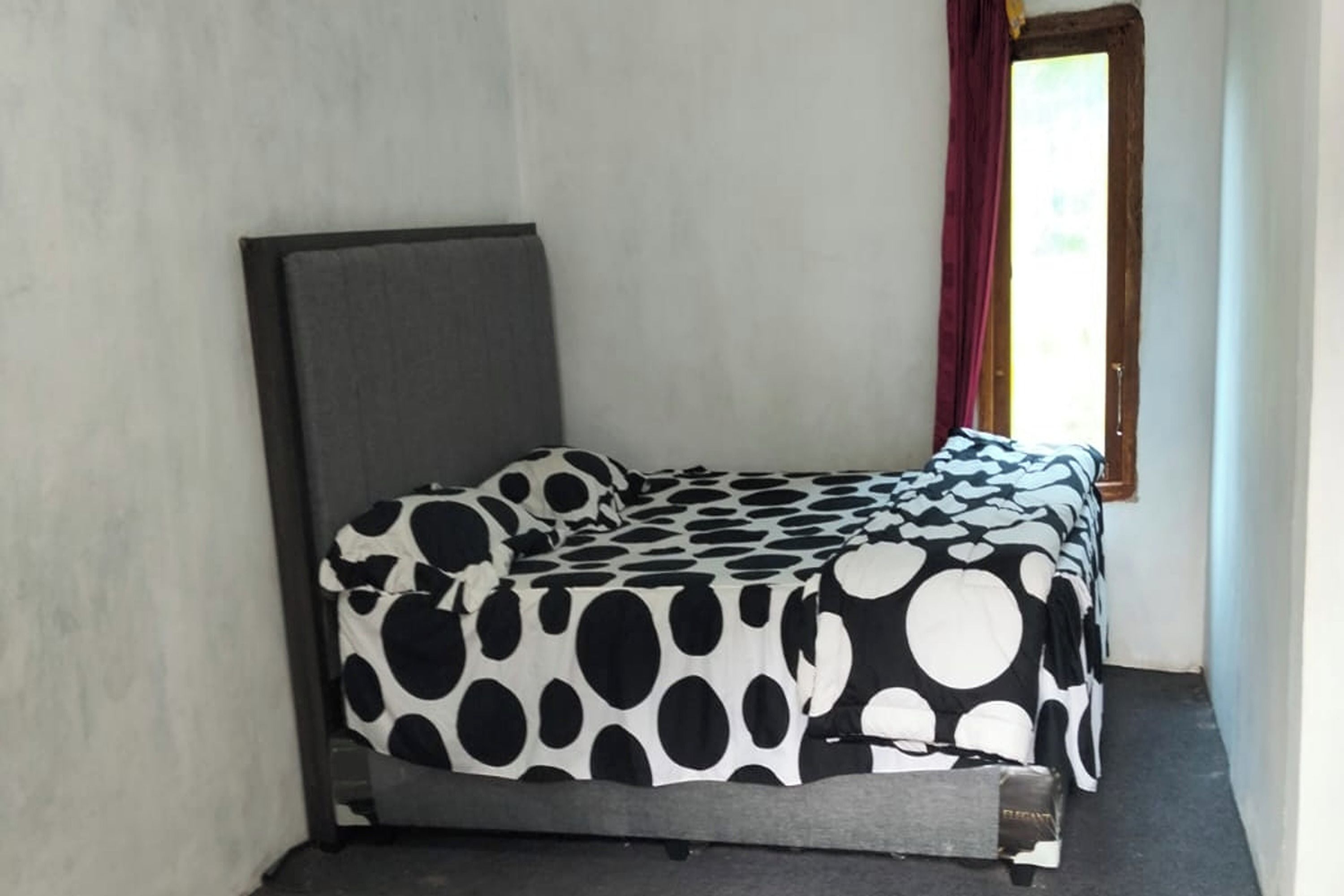 Una cama individual con colcha de lunares blancos y negros en una habitación con ventana y puerta.