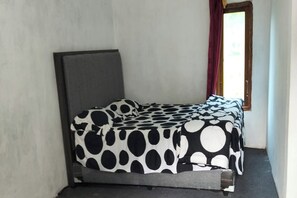 Een eenpersoonsbed met een zwart-wit stippen dekbed in een kamer met een raam en een deur.