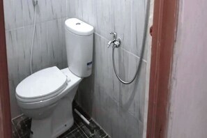 Une petite salle de bain compacte, équipée de toilettes, d’une douche et d’un porte-rouleau de papier toilette fixé au mur.