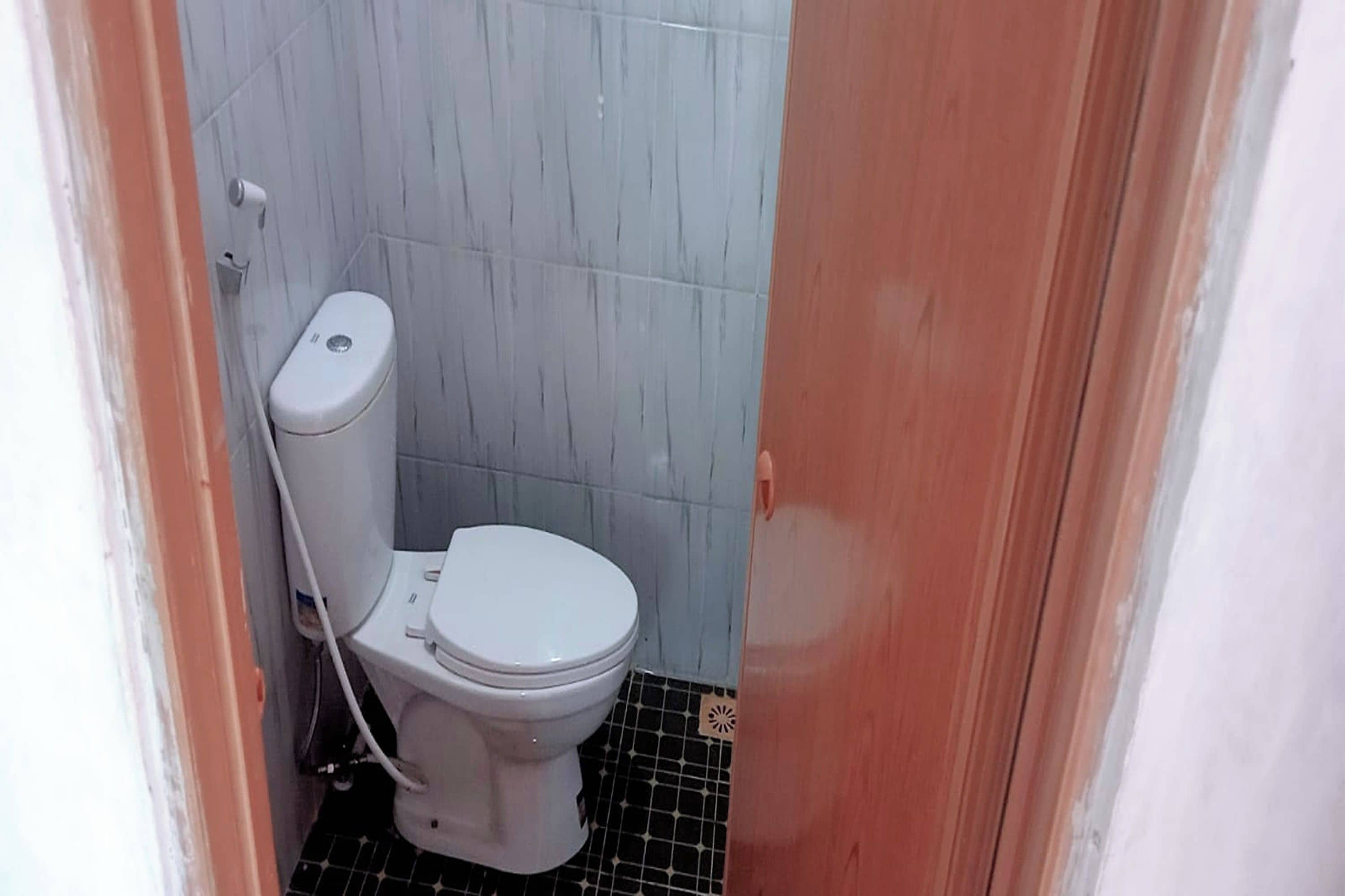 A small bathroom with a white toilet, tiled walls, and a black and white floor.