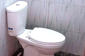 Un inodoro blanco estándar en un baño con paredes de azulejos.