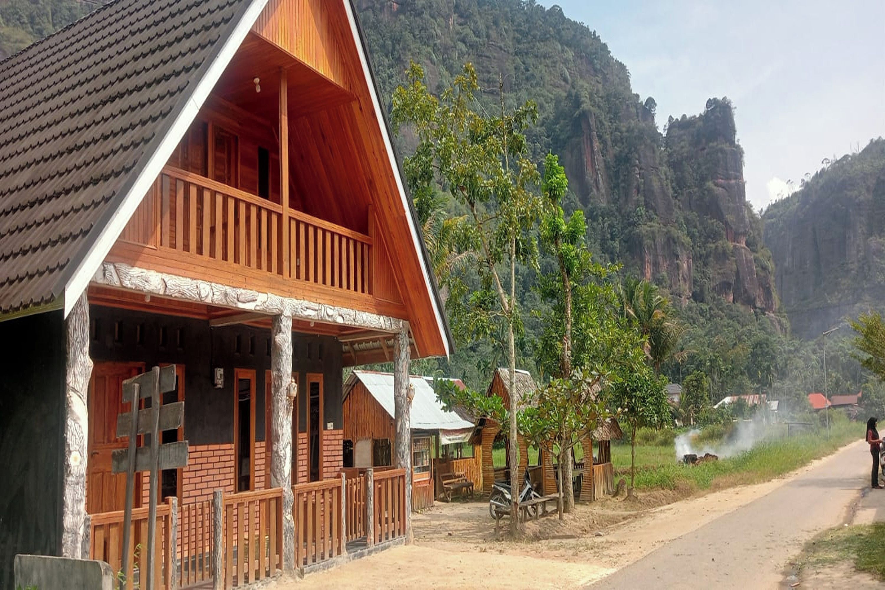 A wooden cabin with a balcony, surrounded by lush greenery and mountains.