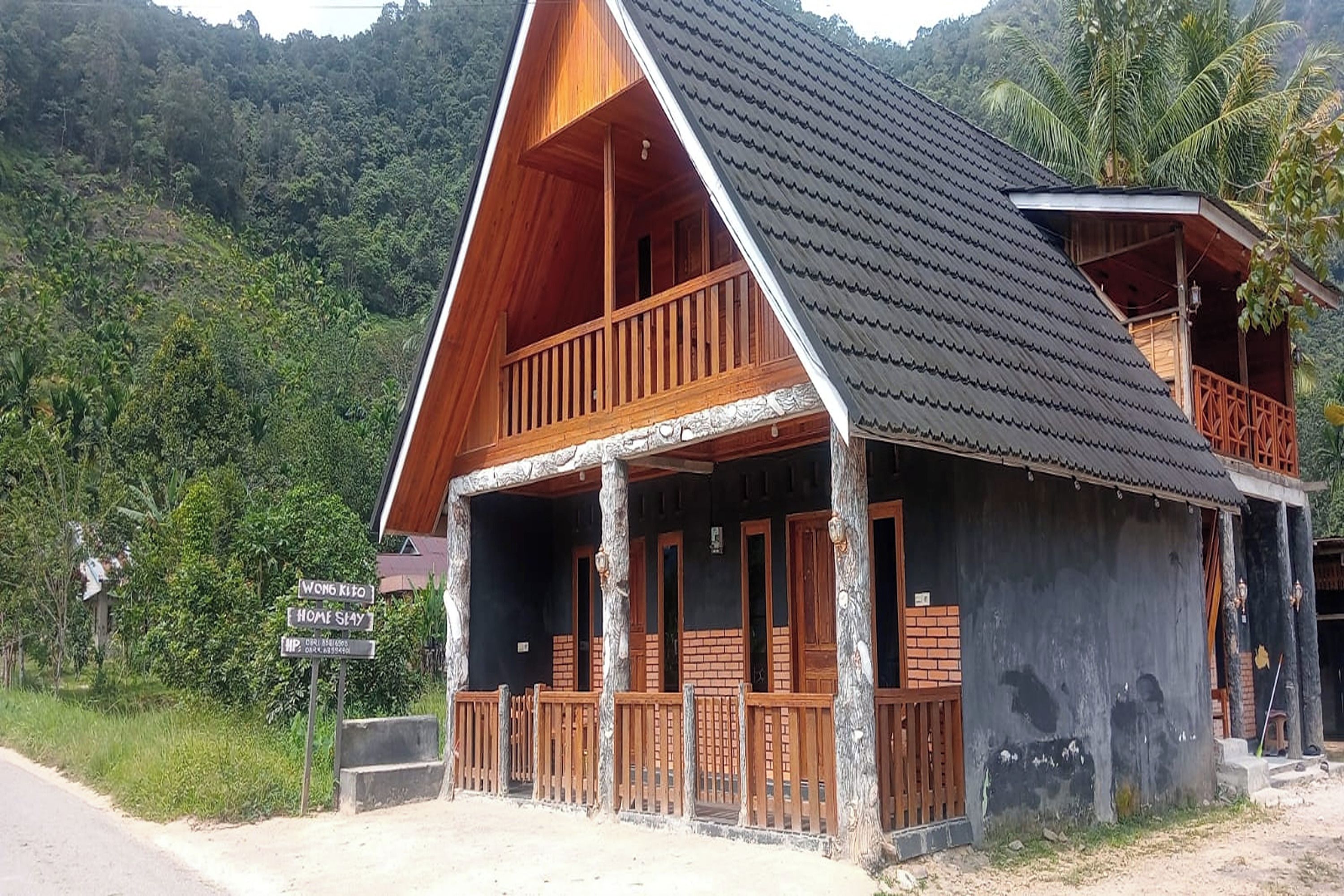 A wooden house with a balcony, surrounded by lush greenery and hills.