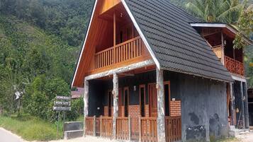 A wooden house with a balcony, surrounded by lush greenery and hills.