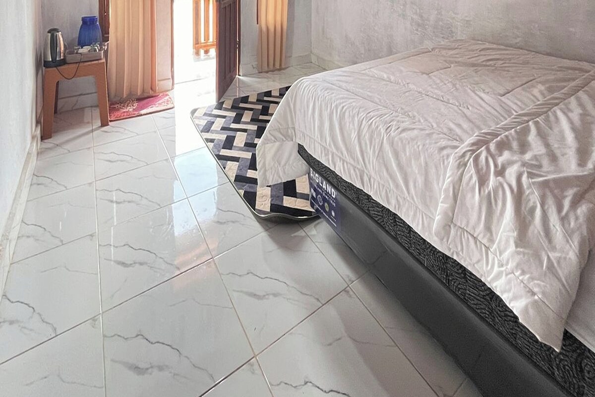 Una habitación de hotel con una cama, una mesita con hervidor y una alfombra estampada.