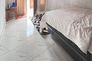 Una habitación de hotel con una cama, una mesita con hervidor y una alfombra estampada.