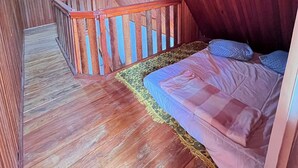 Een kamer met houten vloeren, een bed, een houten leuning en een kamerbreed tapijt met een patroon.