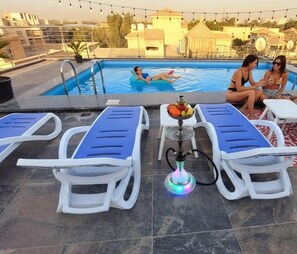 A rooftop pool area with lounge chairs, a hookah, and a view of the surrounding buildings. - Zen Pyramids Luxury Villa (Giza)