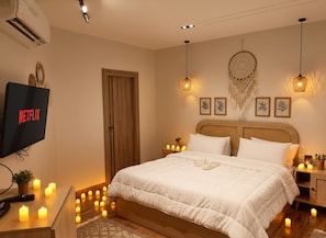 Une chambre à coucher bien rangée, avec un grand lit, des lampes de chevet, des œuvres d’art accrochées au mur et un téléviseur  à écran plat affichant le logo « NETFLIX ».