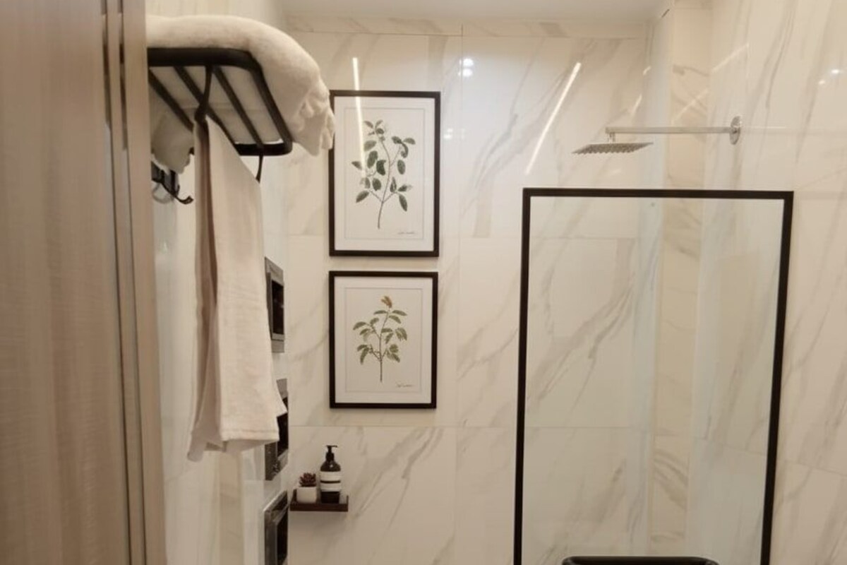 A modern bathroom with a glass shower enclosure, a toilet, and a small shelf with towels.
