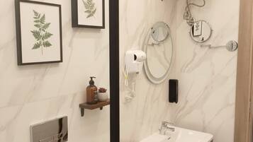 A modern bathroom with a marble wall, a sink, a mirror, a towel rack, and a shower with a handheld showerhead.