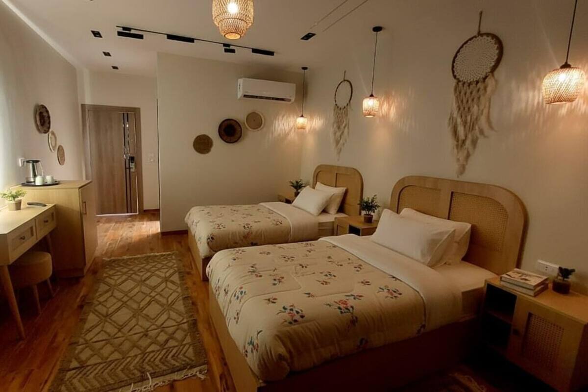 Un dormitorio con dos camas, un escritorio y un espejo. Hay decoraciones en la pared y un atrapasueños.