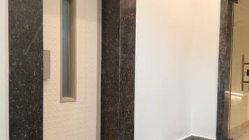 A hallway with a marble floor, a white door with a small window, and a glass door on the right.