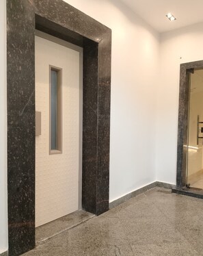 Un corridoio con pavimento in marmo, una porta bianca con una piccola finestra e una porta in vetro a destra.