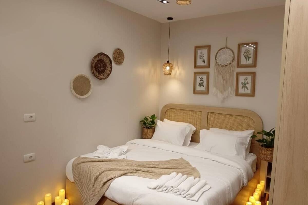 Un dormitorio ordenado con cama, plantas en las mesitas de noche y decoración en la pared.