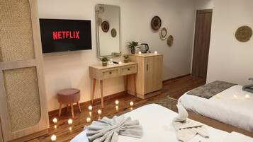 A hotel room with a bed, a bedside table, a mirror, a TV displaying 'NETFLIX', and a wall with decorative plates.