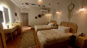 A bedroom with two beds, a desk, and a mirror. There are wall decorations and a dreamcatcher.